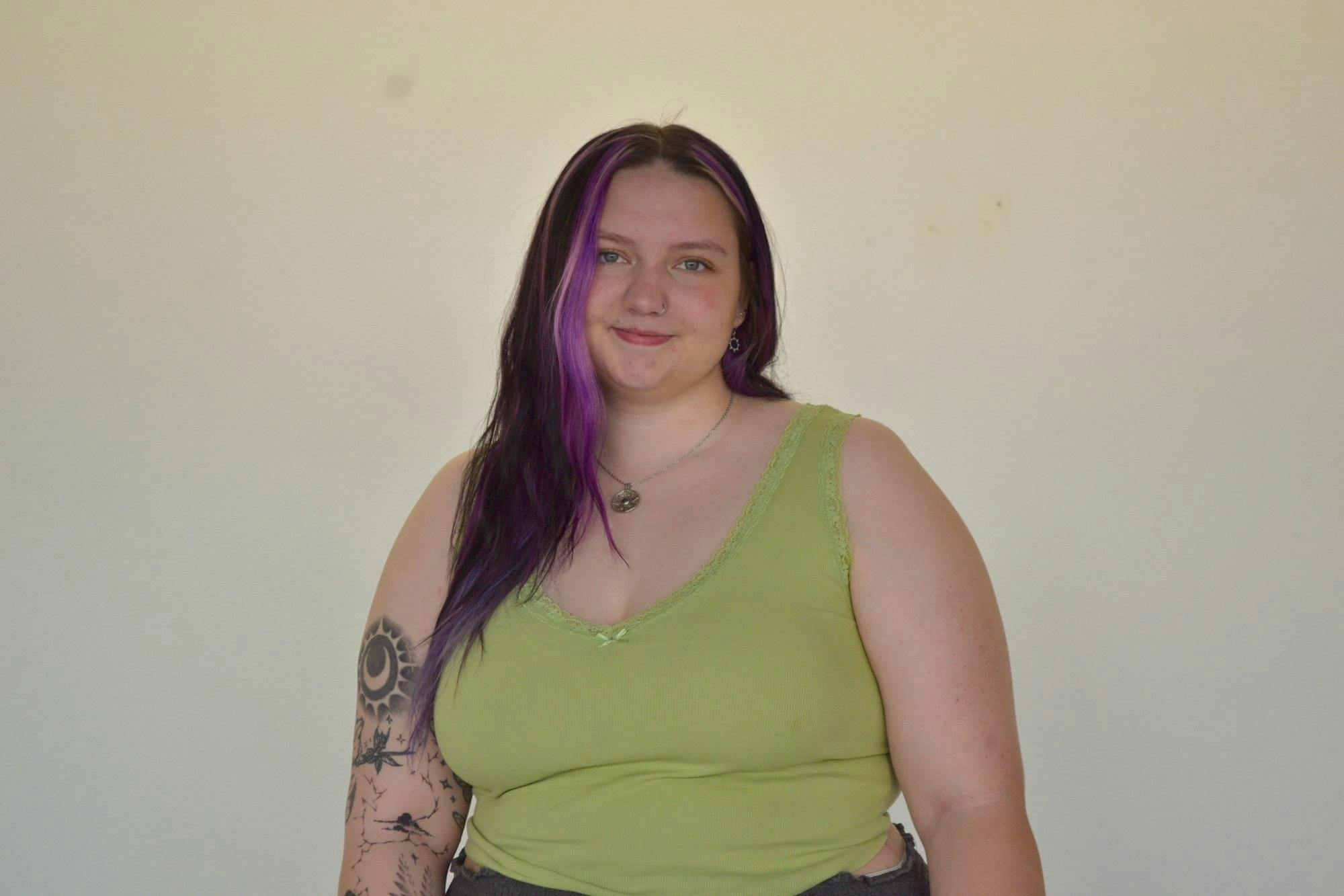 Chrissy Kuiper from the waist up, smiling in front of a blank wall at the camera.