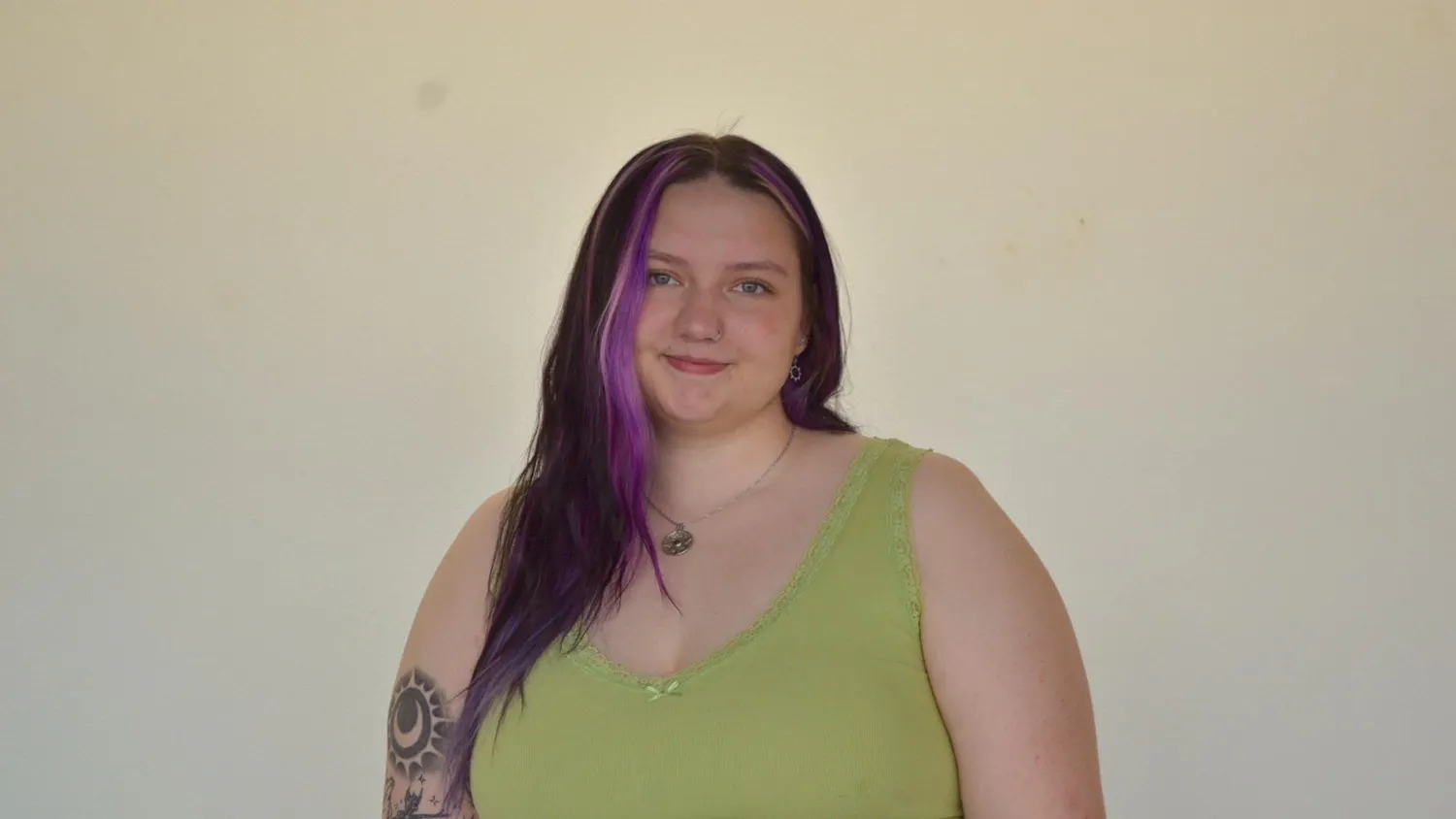 Chrissy Kuiper from the waist up, smiling in front of a blank wall at the camera.