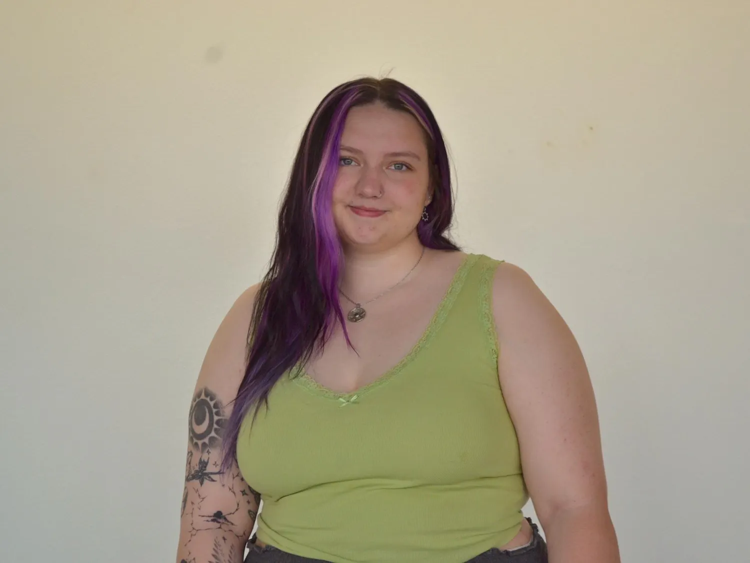 Chrissy Kuiper from the waist up, smiling in front of a blank wall at the camera.