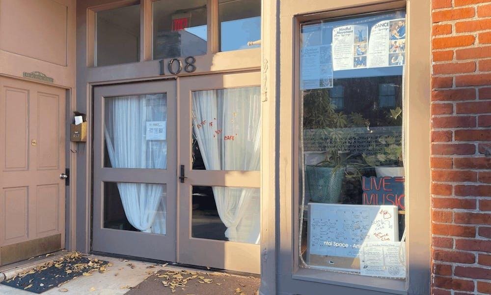 The entrance of a building with double glass doors. The doors are clear, and white curtains on the inside are visible through them. The number "108" is written in silver above the doors. 