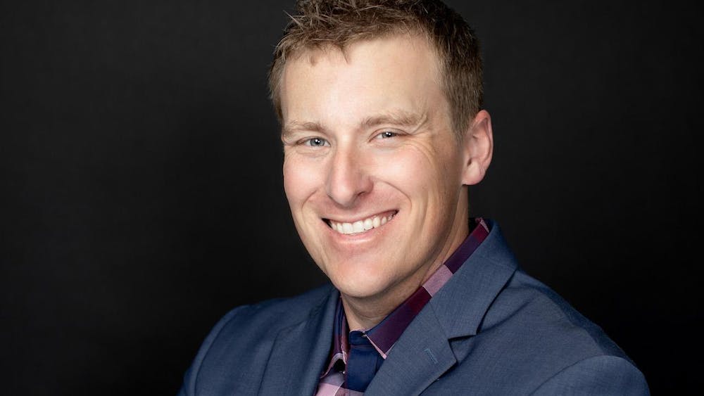 Headshot of Nathan Bomey, from the chest up, smiling with his arms crossed and wearing a gray suit jacket.