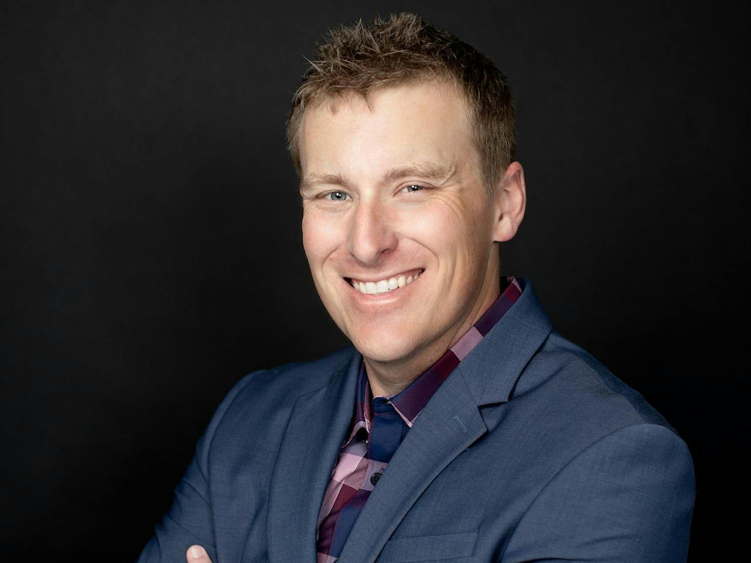 Headshot of Nathan Bomey, from the chest up, smiling with his arms crossed and wearing a gray suit jacket.