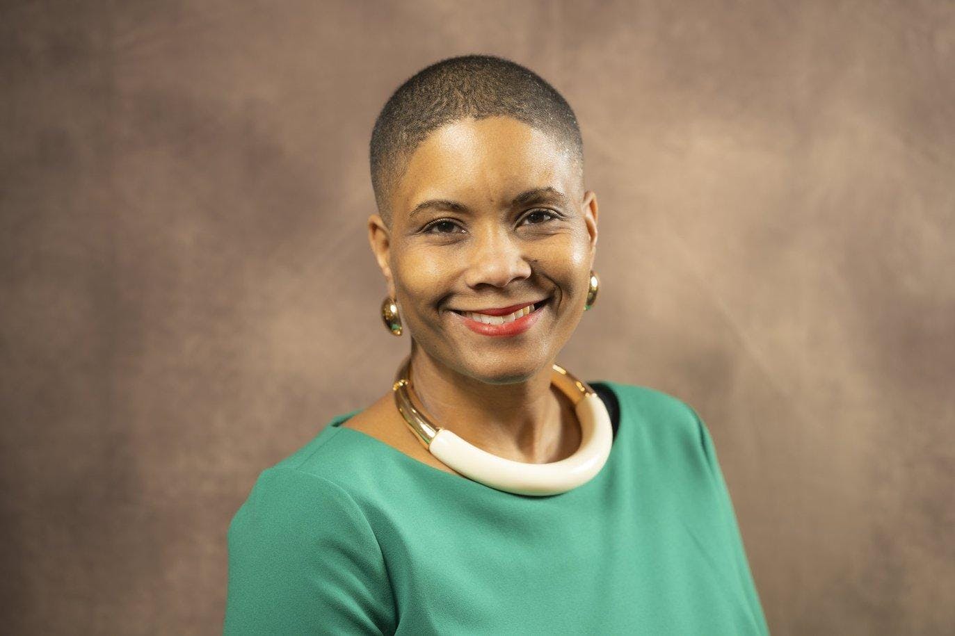 Headshot of Renee' T. Watson from the shoulders up, smiling and wearing a green blouse and gold jewelry.