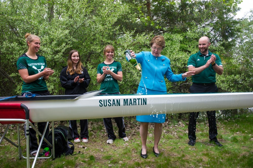 President Susan Martin christens the new eight-oared racing shell named after her, flanked by members of EMU's rowing team.