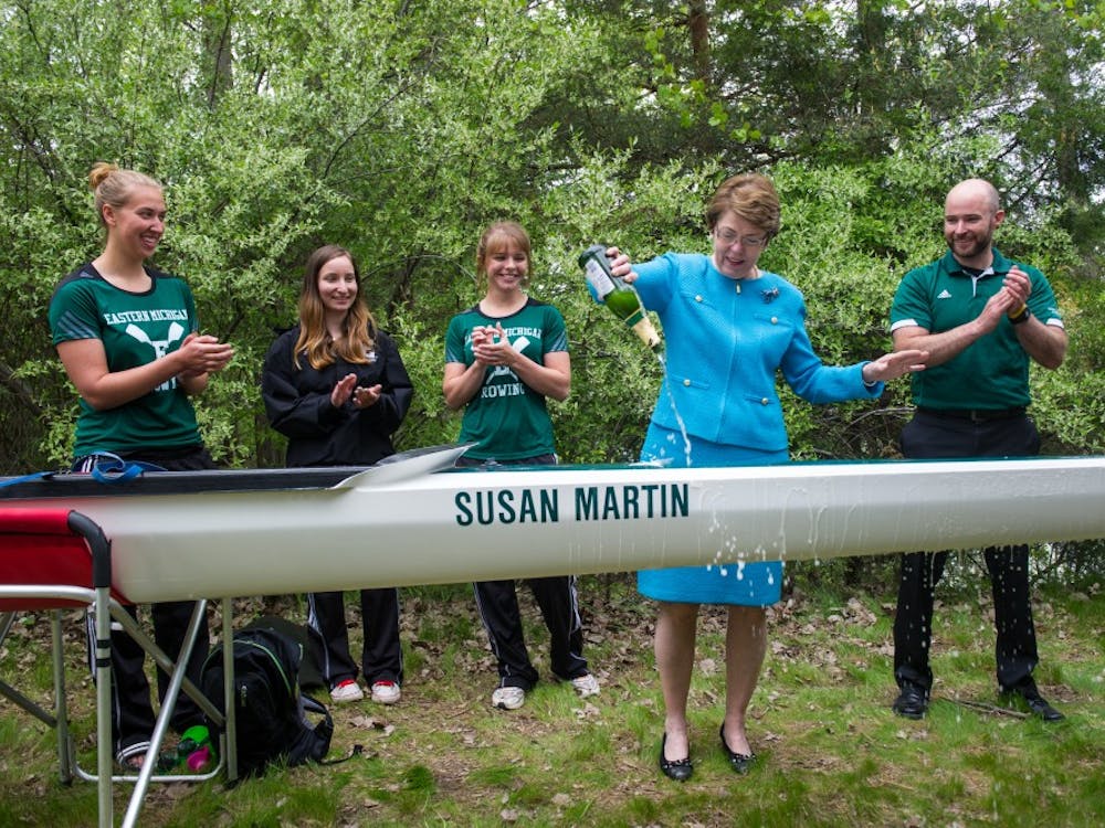 President Susan Martin christens the new eight-oared racing shell named after her, flanked by members of EMU's rowing team.