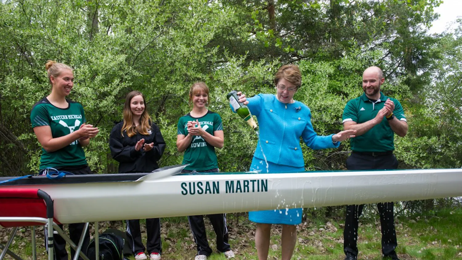 President Susan Martin christens the new eight-oared racing shell named after her, flanked by members of EMU's rowing team.