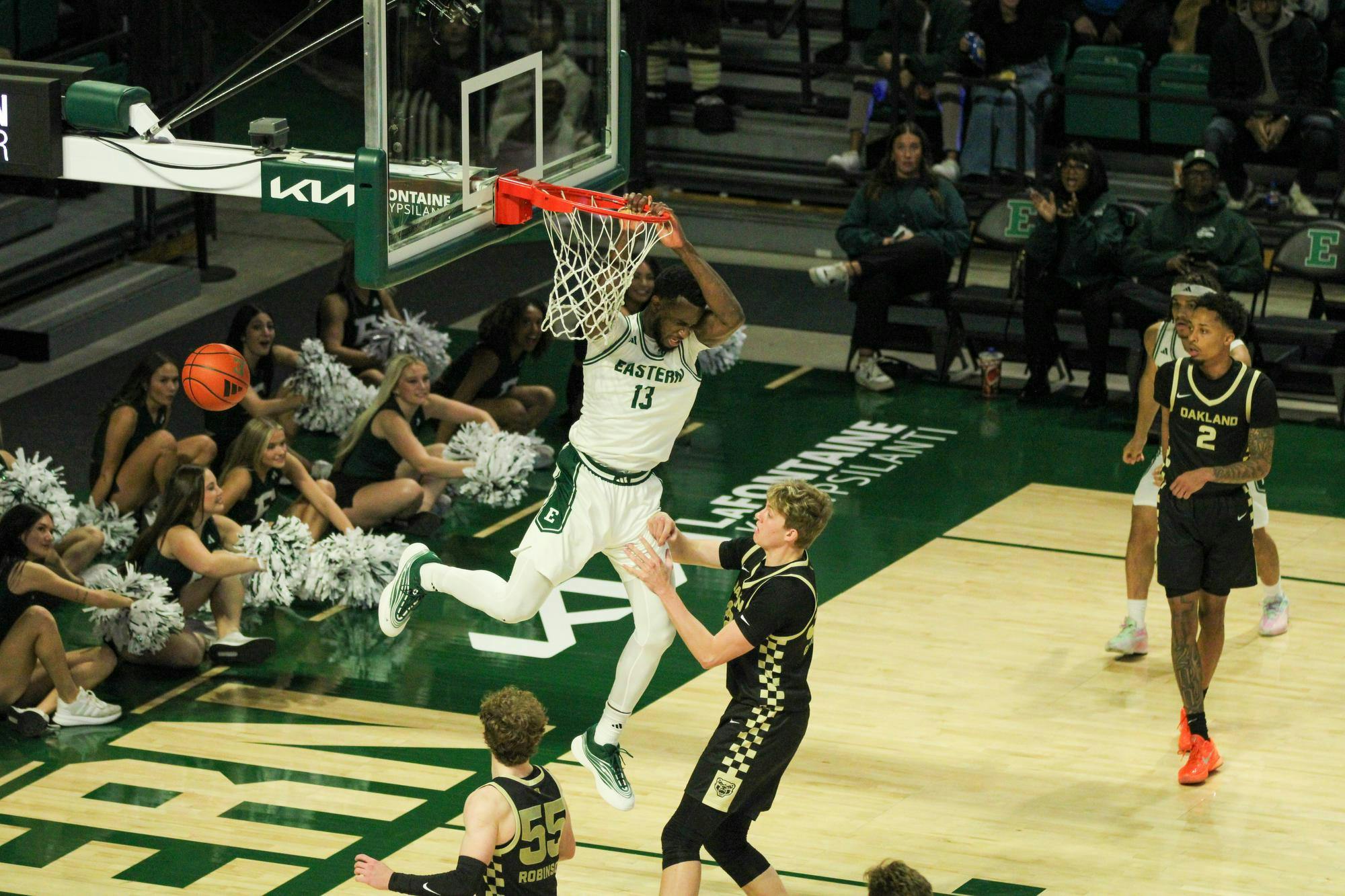 #13, hanging onto the basketball hoop, in a white jersey, over an Oakland player, in a black jersey. 