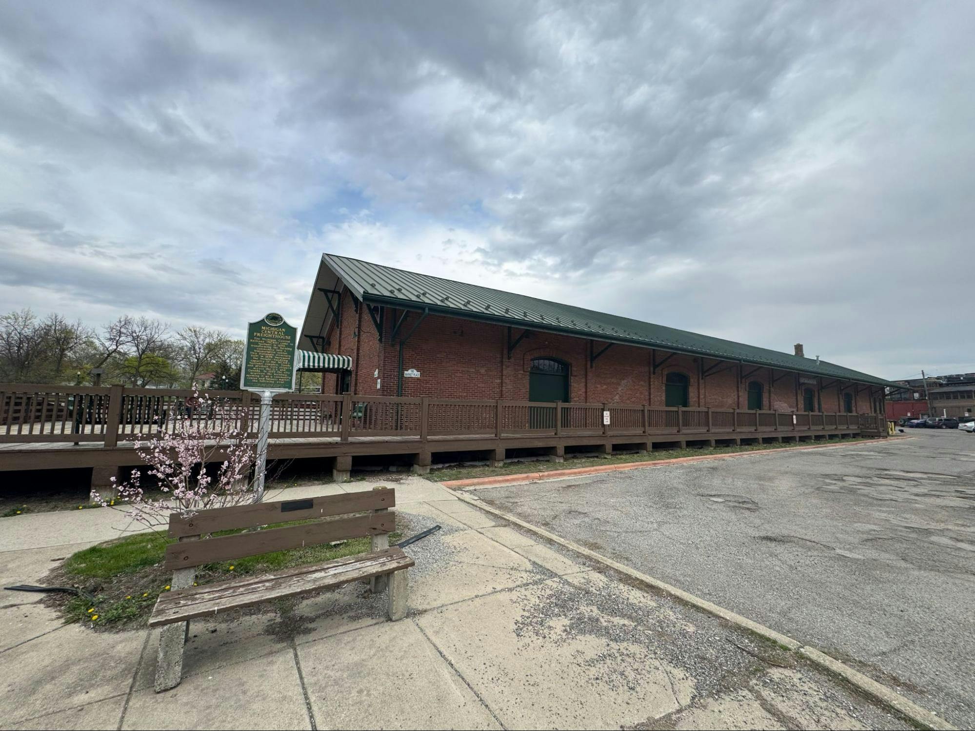 Photo of a brick building with a green roof set behind sidewalk and a parking lot.