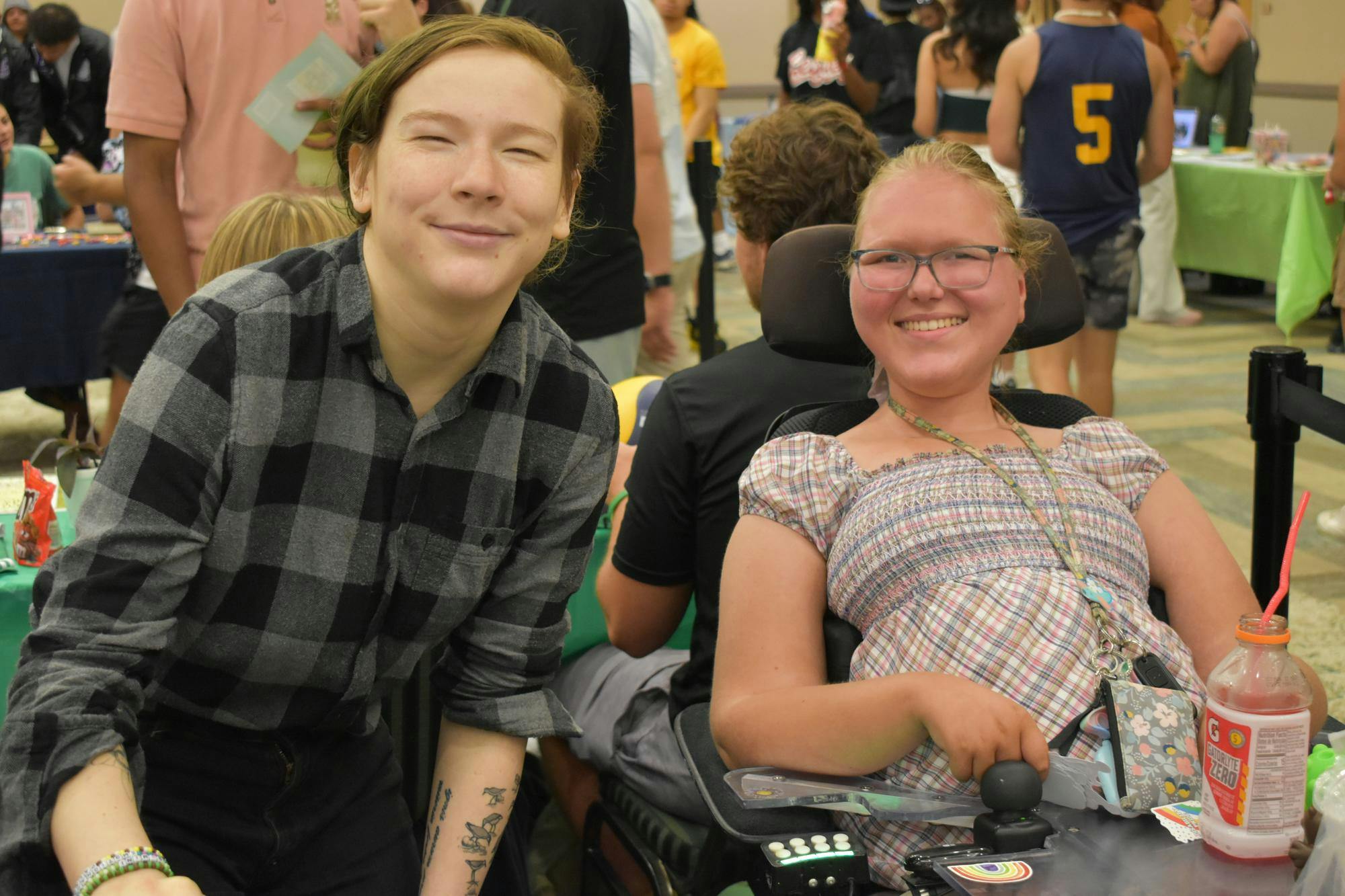 One person crouches next to another in a wheelchair and both are smiling.