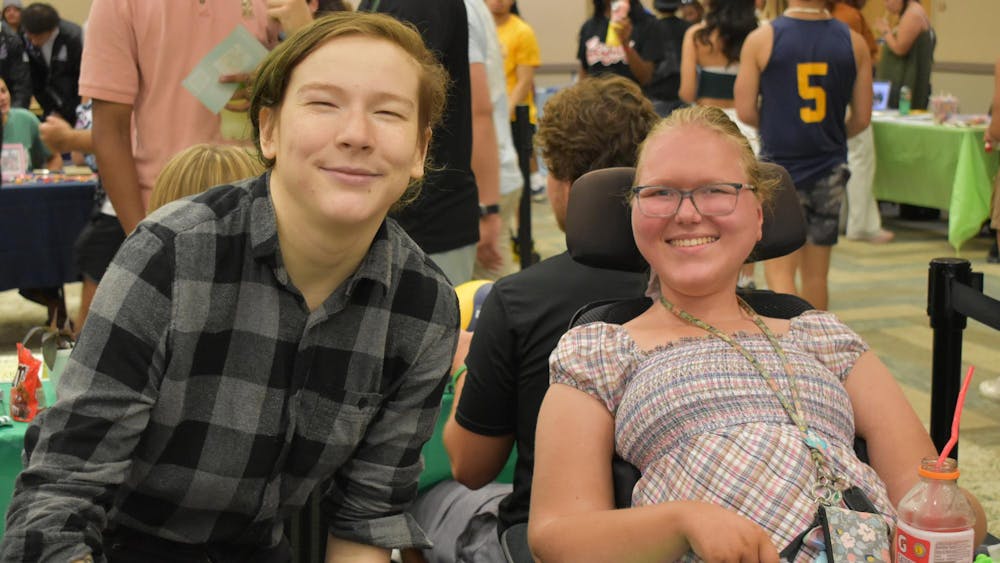 One person crouches next to another in a wheelchair and both are smiling.