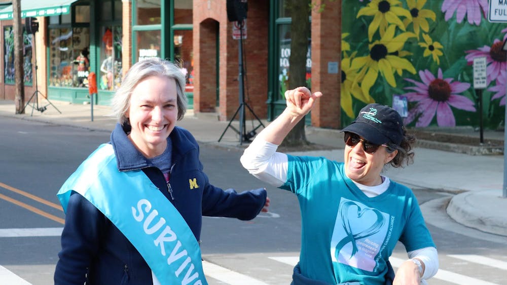 Two women celebrate and smile while wearing blue shirts for the event, with the leftmost wearing a teal survivor ribbon as a sash across her chest.