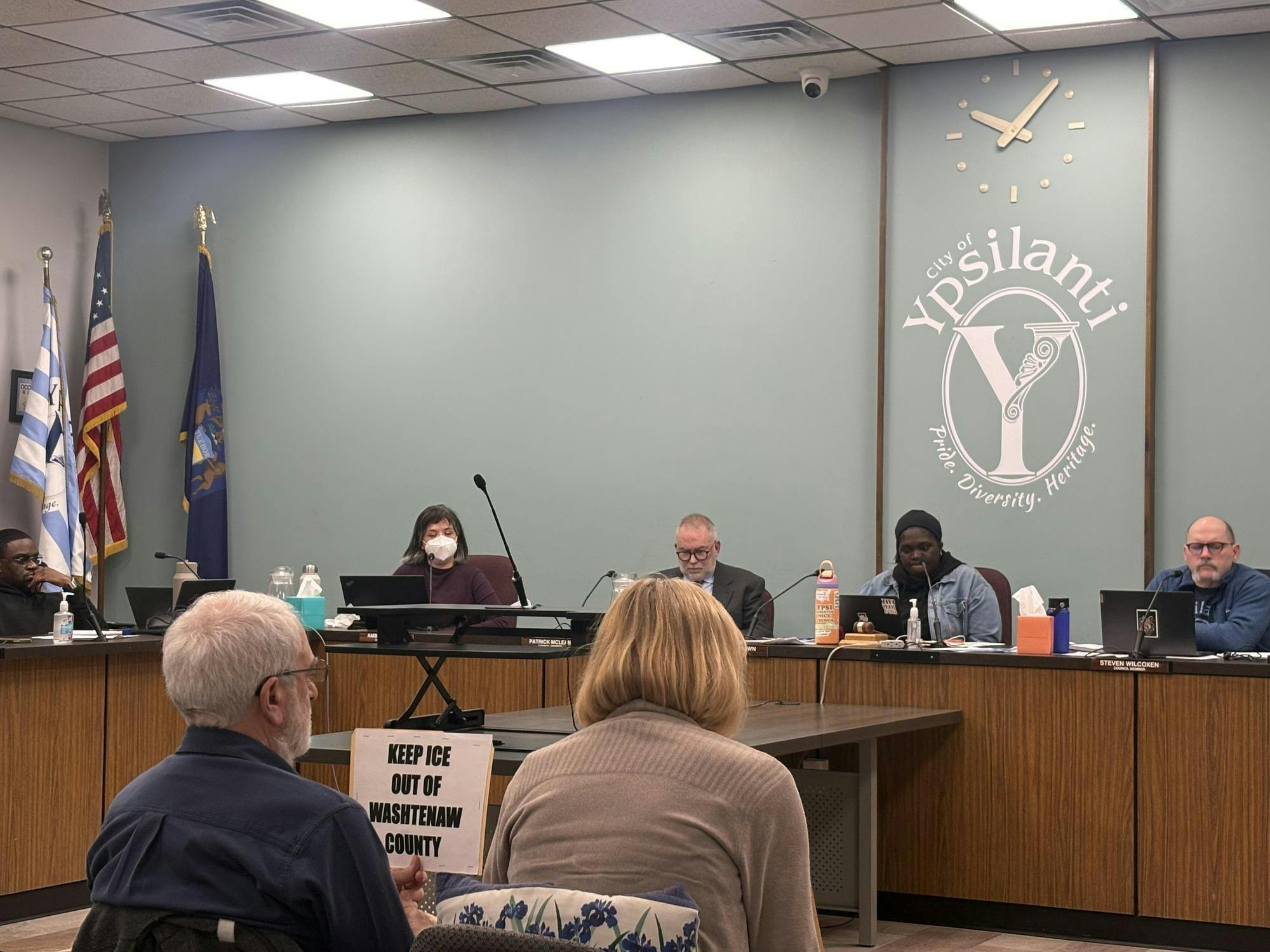 The back of two attendees in City Hall's Council Chambers watching on as councilors discuss a resolution. 
