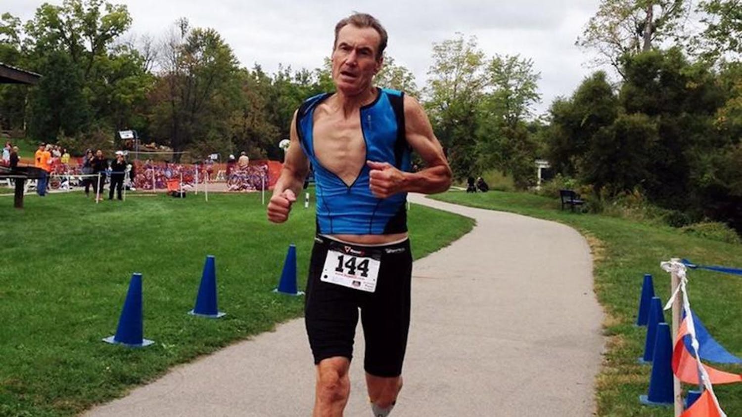 Derrick Fries, a white man with short hair, running in black shorts and a blue shirt with the number '144' pinned to him.