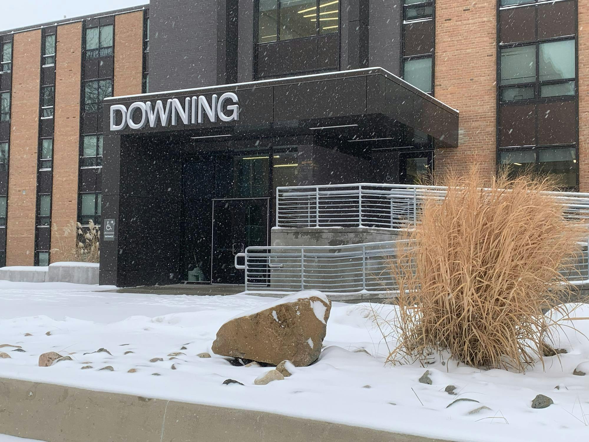 Red brick building with brown metal trim and glass windows. The entrance has an accessibility ramp with metal railings and a roof over the doors reading "Downing."