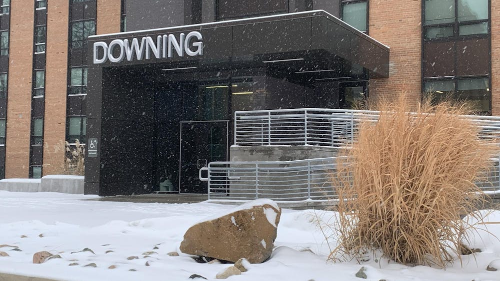 Red brick building with brown metal trim and glass windows. The entrance has an accessibility ramp with metal railings and a roof over the doors reading "Downing."