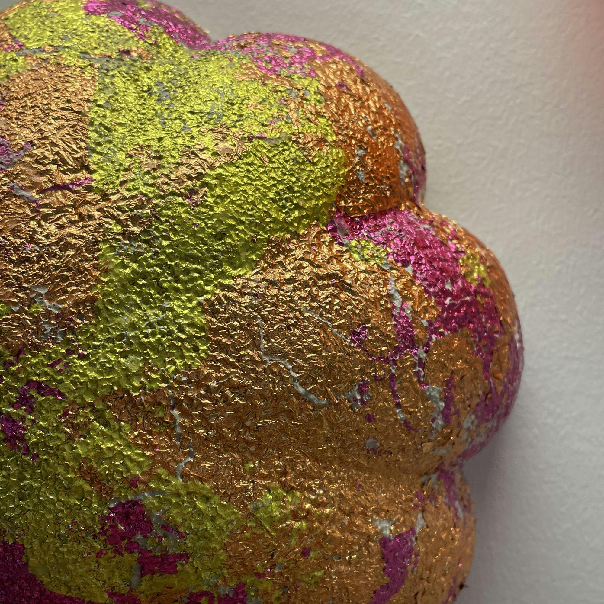 Close-up of textured 3D artwork. It is shaped like a flower and is pink, yellow, and orange with a shiny, rough texture.