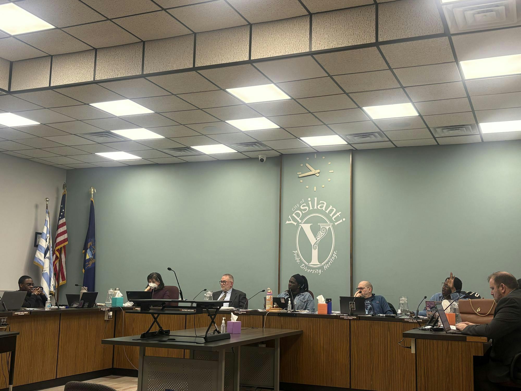 A group of council members sitting behind a table in front of a wall with a city of Ypsilanti logo in the middle. 