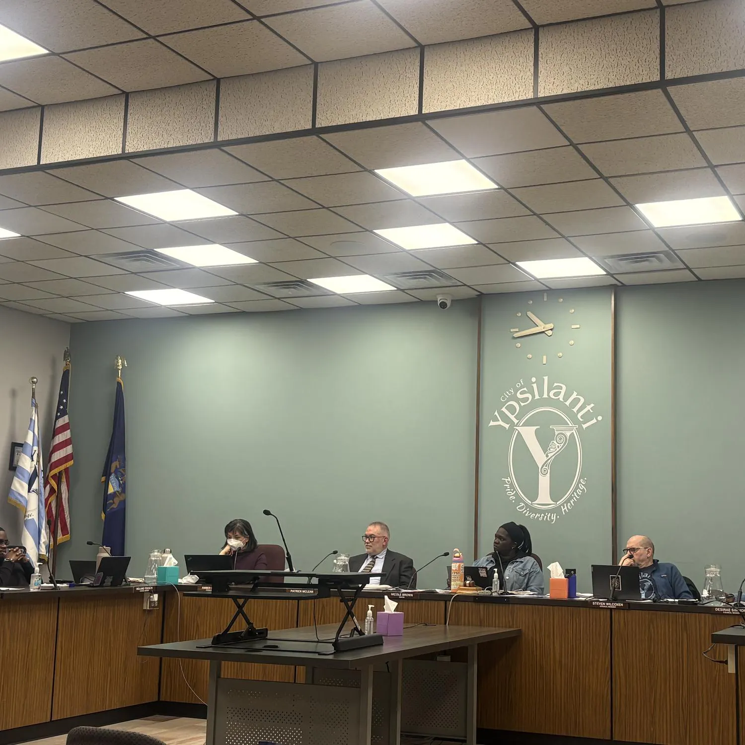 A group of council members sitting behind a table in front of a wall with a city of Ypsilanti logo in the middle.