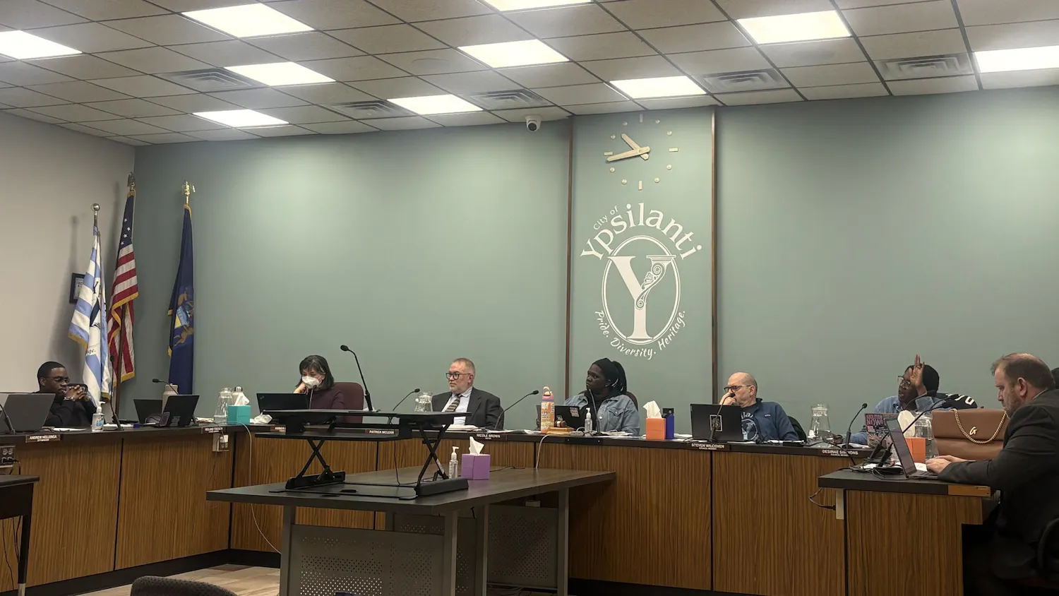 A group of council members sitting behind a table in front of a wall with a city of Ypsilanti logo in the middle.