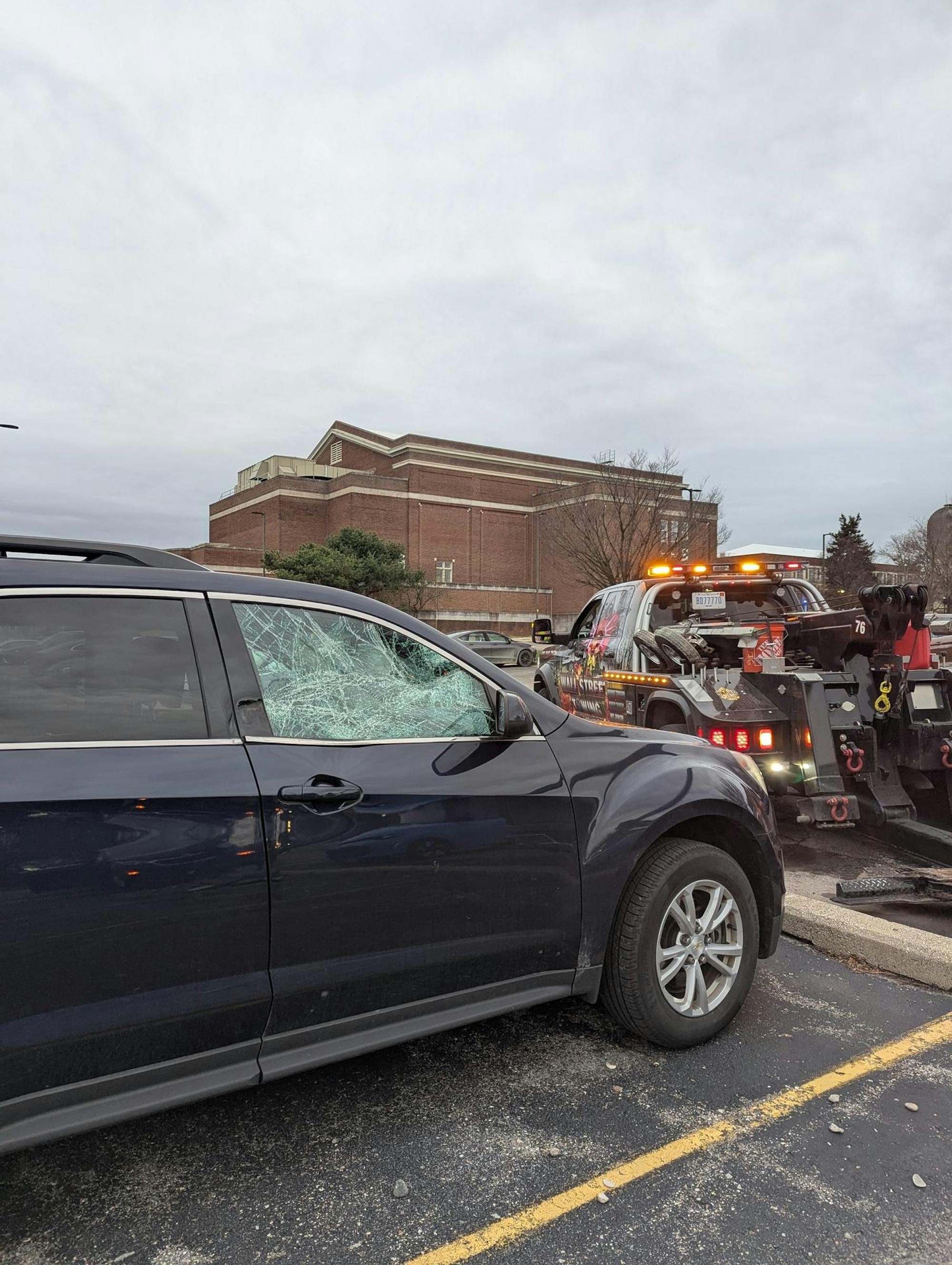 A car with a broken window with a tow truck behind it.