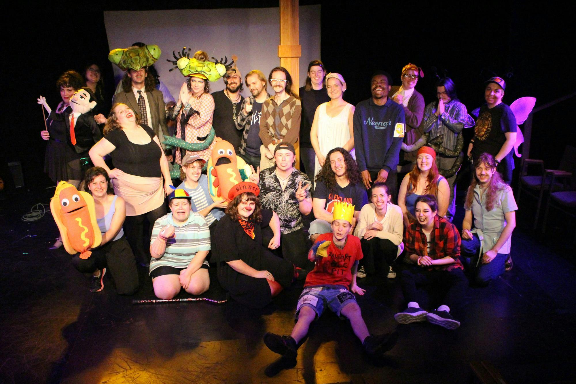 An ensemble of actors, puppets, musicians and stage hands pose for a photo on a stage.
