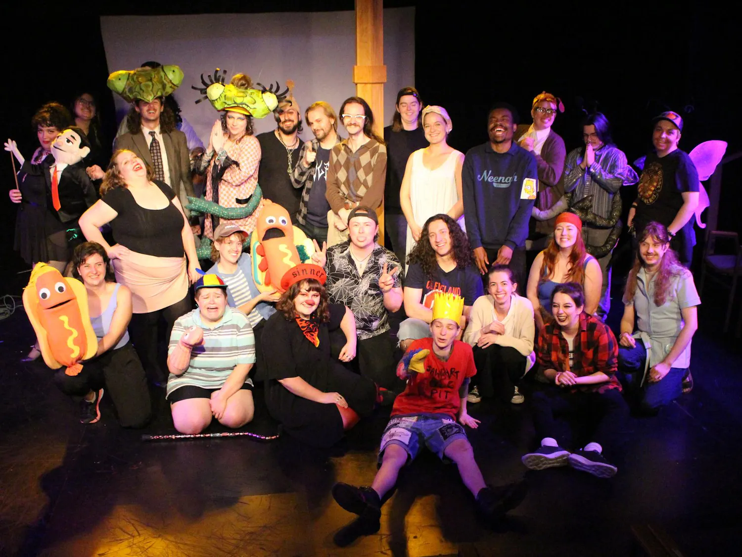 An ensemble of actors, puppets, musicians and stage hands pose for a photo on a stage.