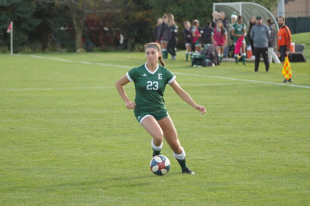 Lindsey Shira is shown mid-run with the soccer ball just in front of her left foot. She is the only player visible on the field.
