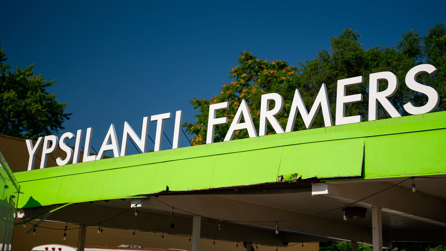 White letters, spelling out Ypsilanti Farmers, line the top of a bright yellow canopy over the area that is home to the Ypsilanti Farmers Market.
