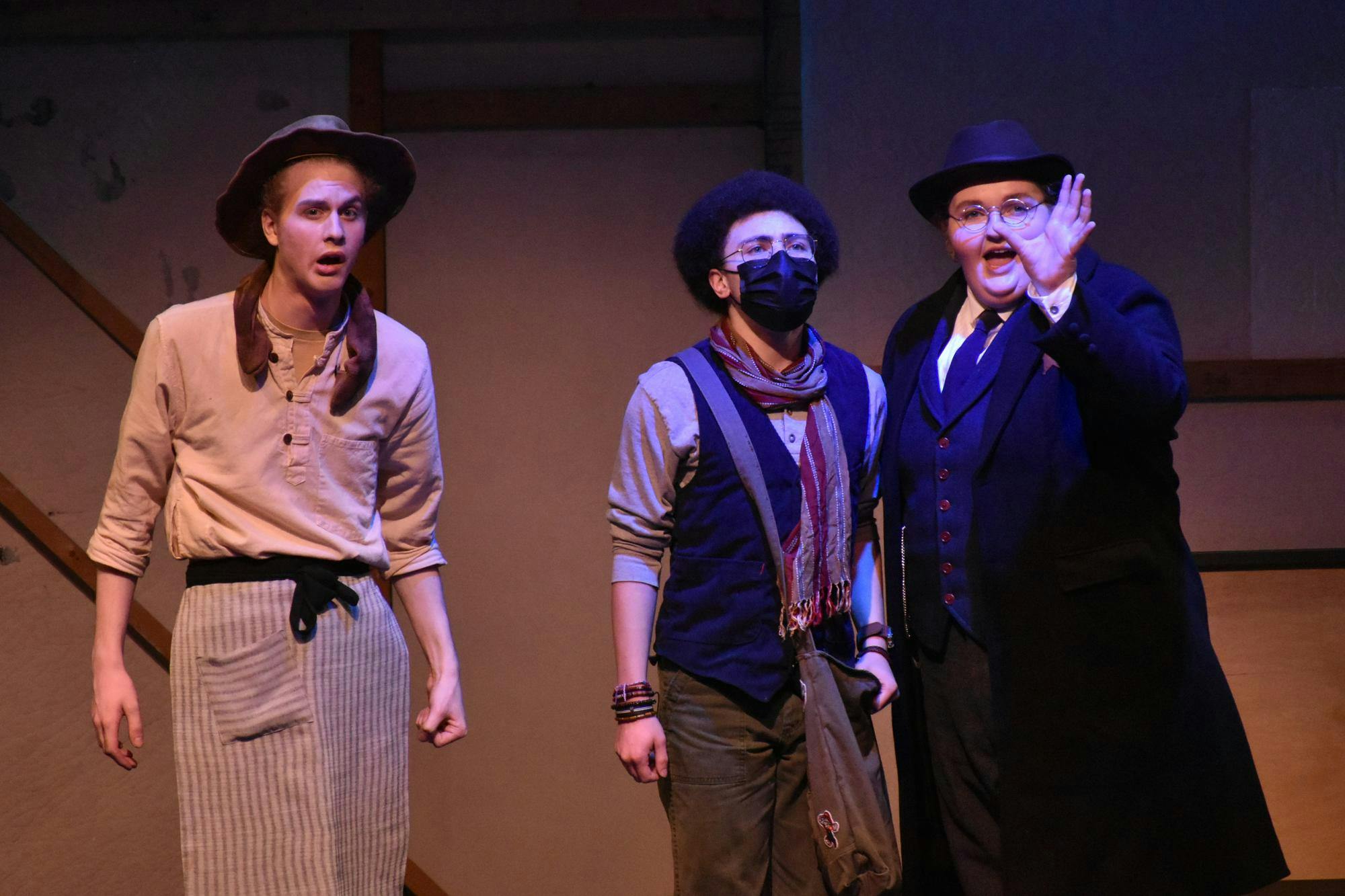 Three actors stand on stage in vintage clothing, two of them speaking to each other while the other looks off into the distance.