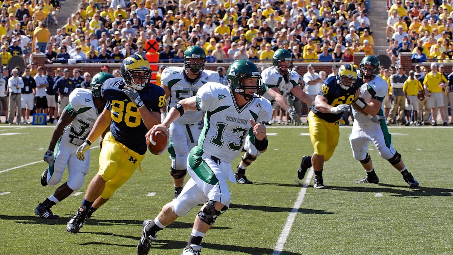 Alex Gillett (13) under pressure from linebacker (88) Craig Roh during EMU’s 45-17 loss to Michigan on Sept. 19 when he filled in for the injured Andy Schmitt. Gillett will share playing time with Kyle McMahon on Saturday, coach Ron English said.