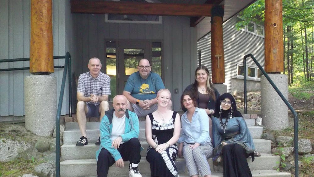 7 adults sit on concrete stairs outdoors in front of a gray building.