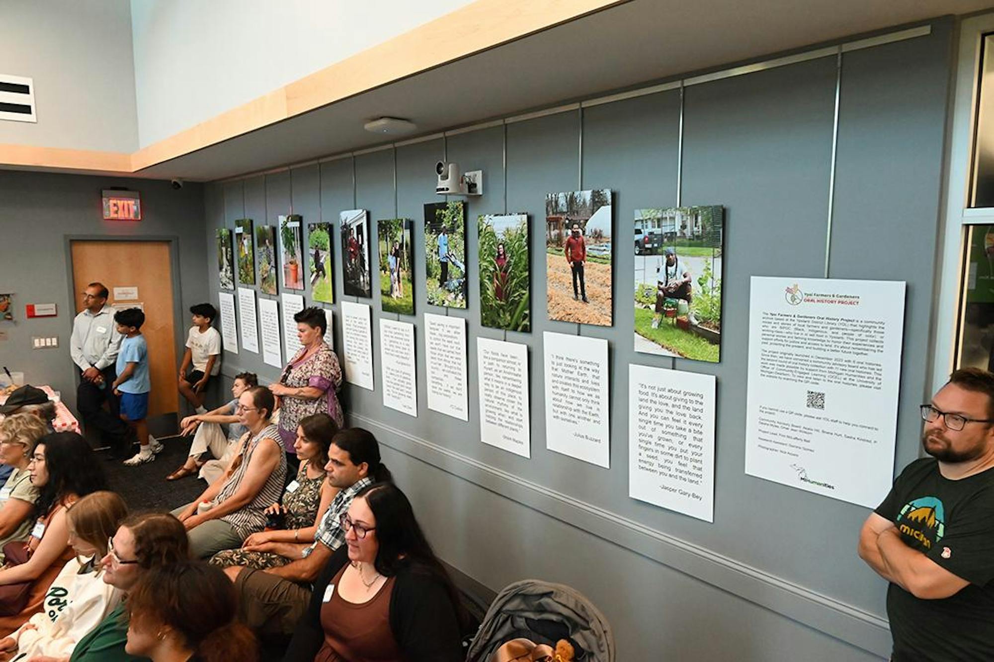 Attendees gather in a room; hanging on the wall are photos of gardeners for the oral history exhibit.