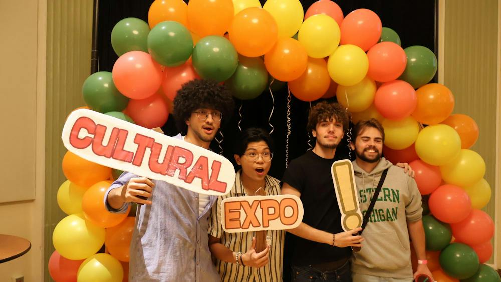 Four students pose in front of a balloon arch and hold signs that say "Cultural Expo!"