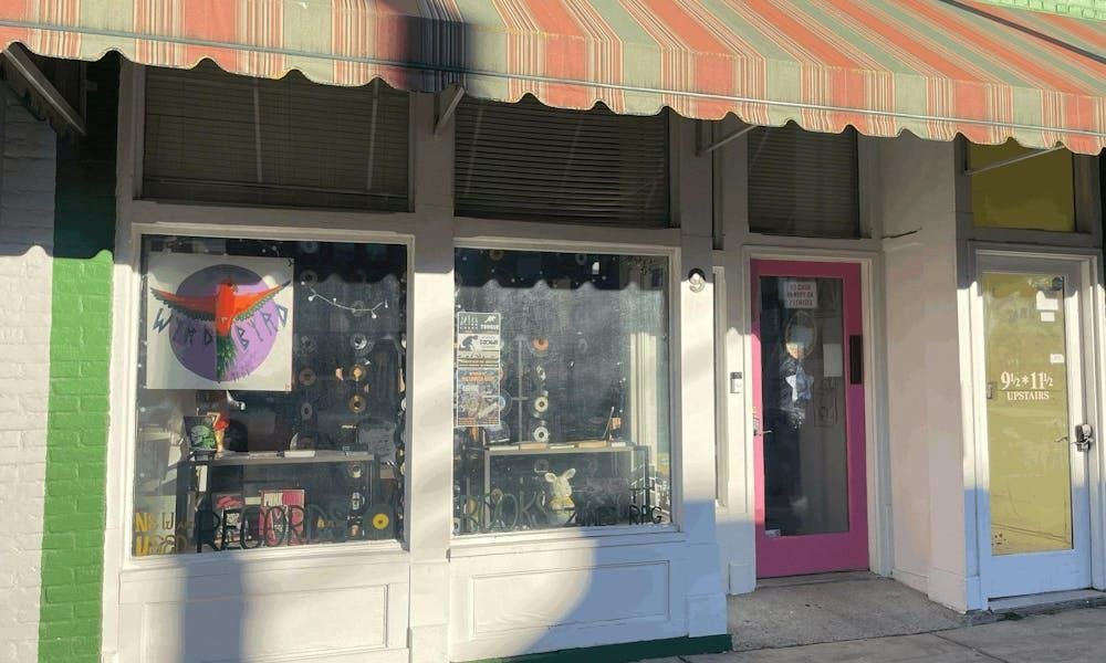 White-painted storefront with large windows and a green and red awning above the entrance. Vinyl records hang in the window with a sign reading "Wyrd Byrd."