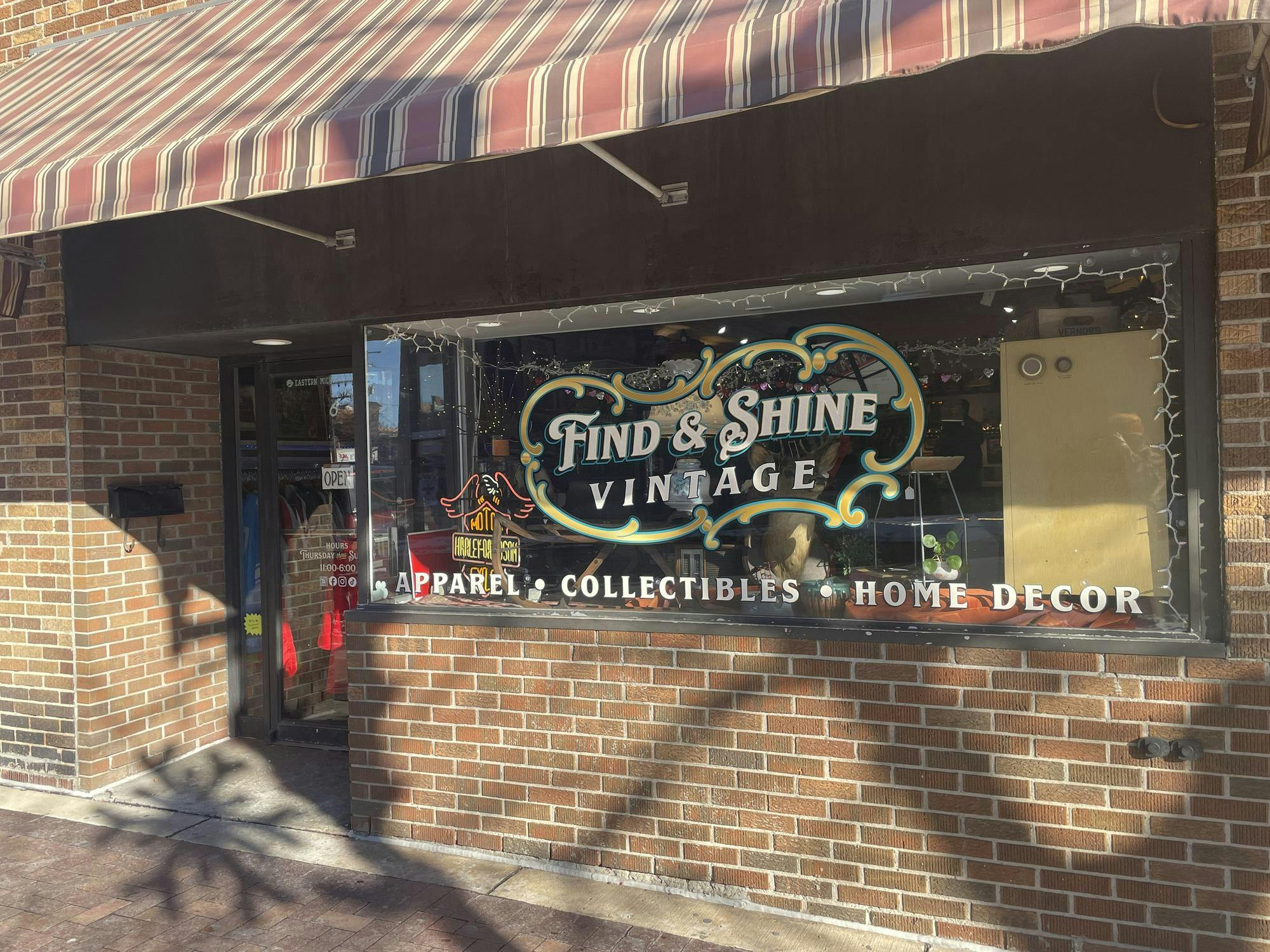 A brick building with a large window, displaying the logo for Find & Shine Vintage, and a red, brown and yellow striped awning.