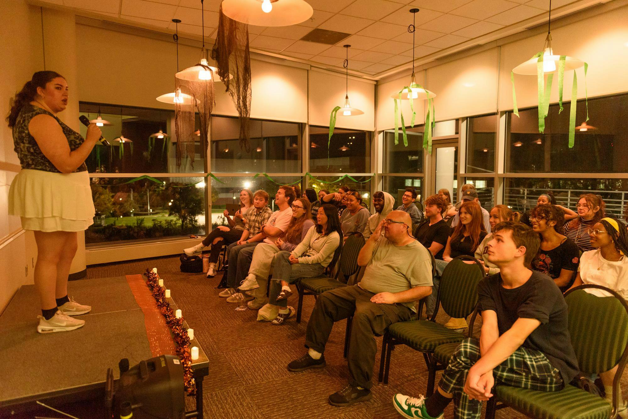 A person standing on a stage talks to the crowd as they all start laughing hysterically at her commentary.