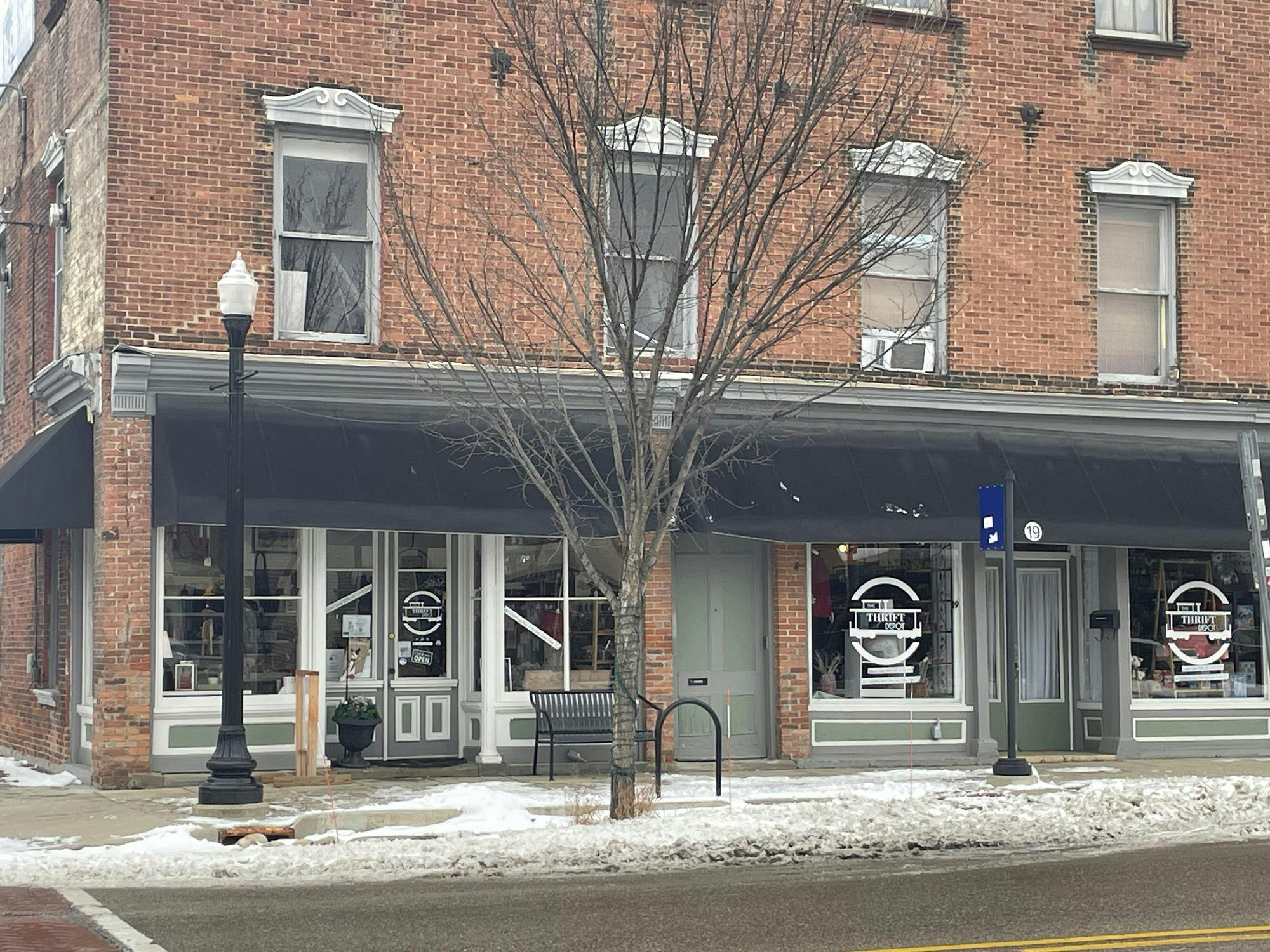 A large brick building with a black awning and a bare tree and light post in front of it.