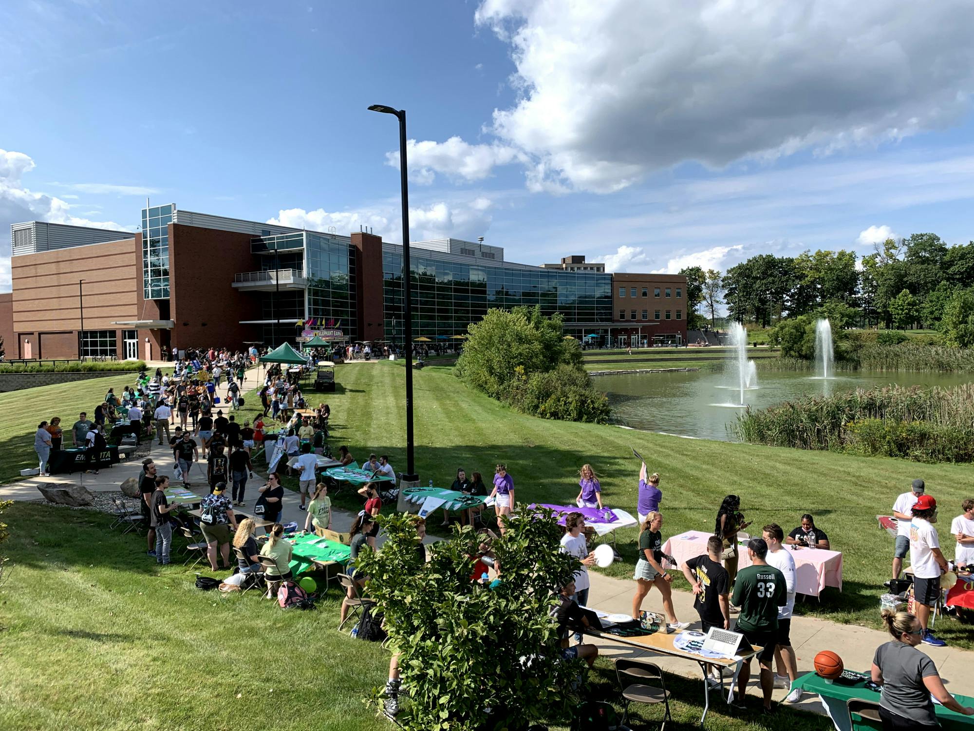 Tables from varying student organizations line the sidewalk in front of the Student Center. Many students walk the sidewalk between the tables.
