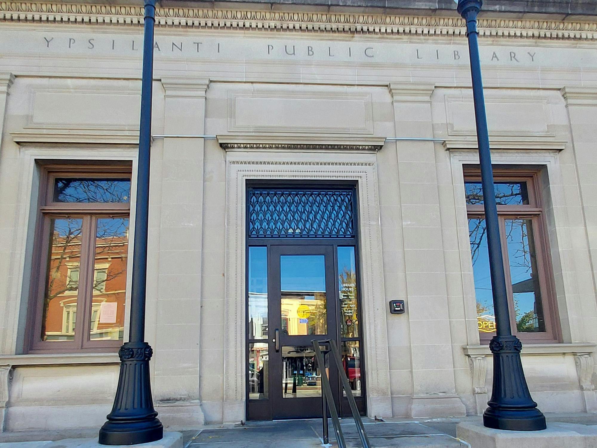 In downtown Ypsilanti, the front entrance of the Ypsilanti Public Library, located on Michigan Avenue, features a glass door and large rectangular windows on both sides.