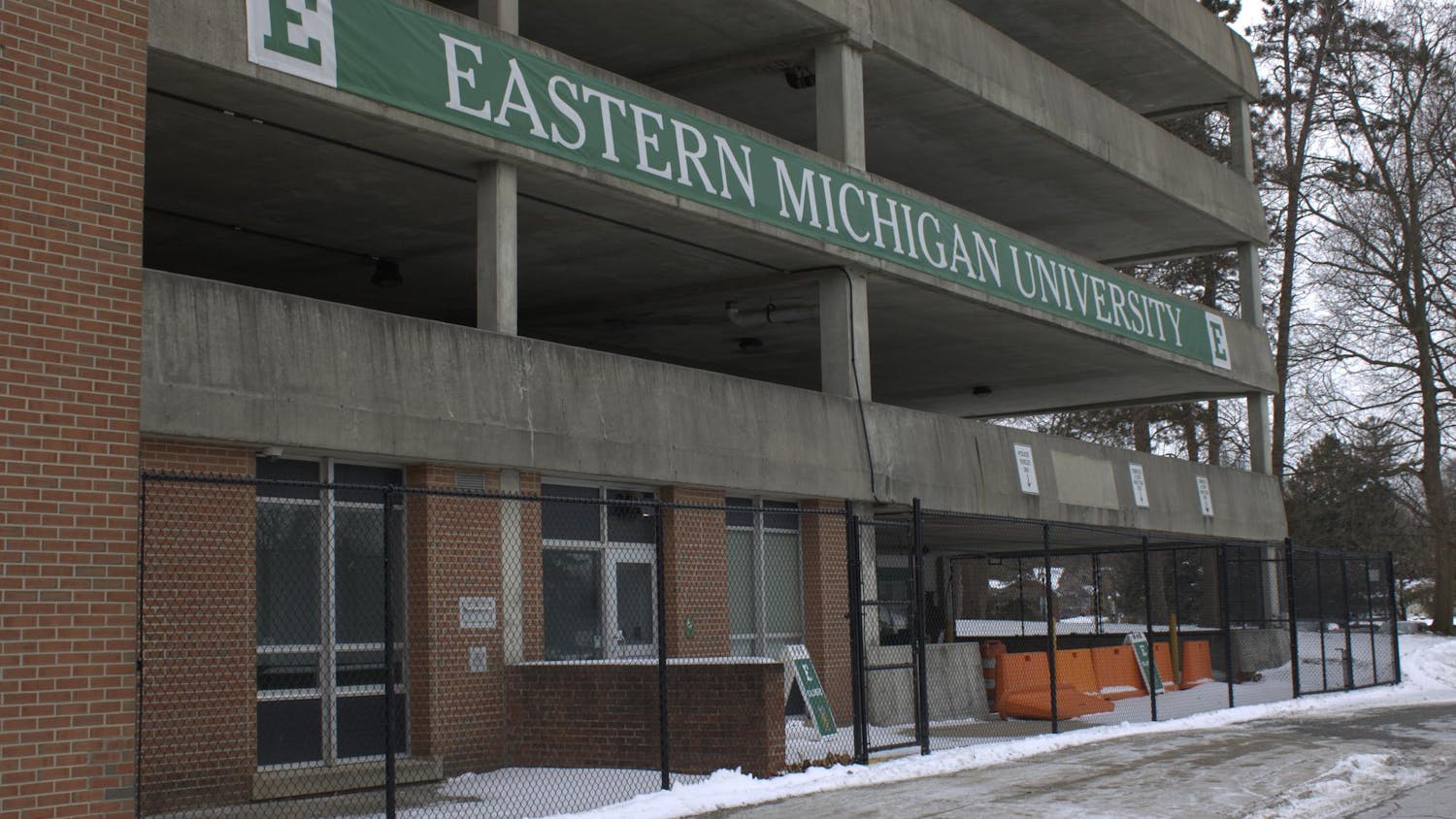 Black metal chain-link fencing outside a brick and cement multi-level parking garage.