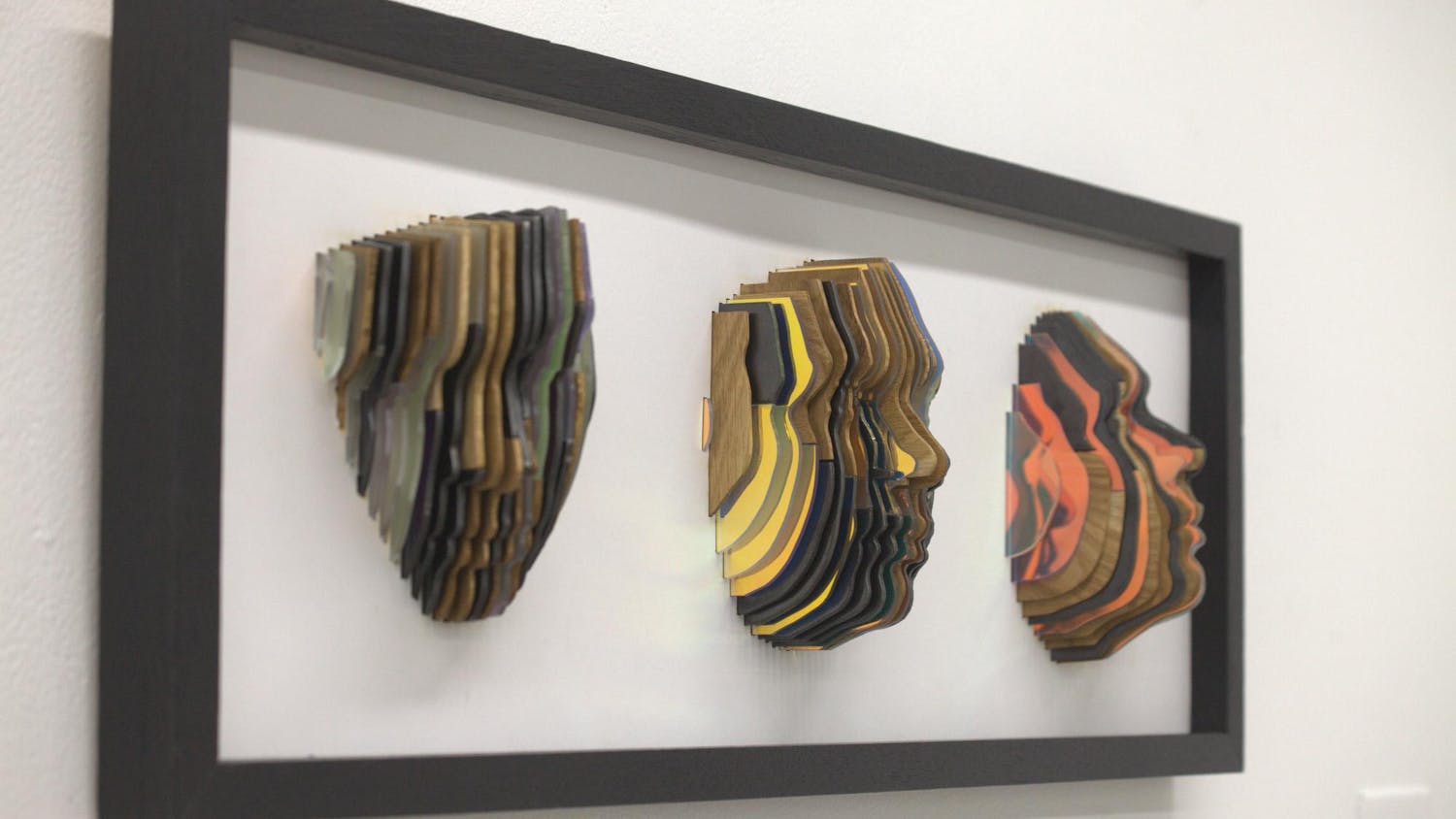 Three faces made of vertical wood, metal, and plastic slices.