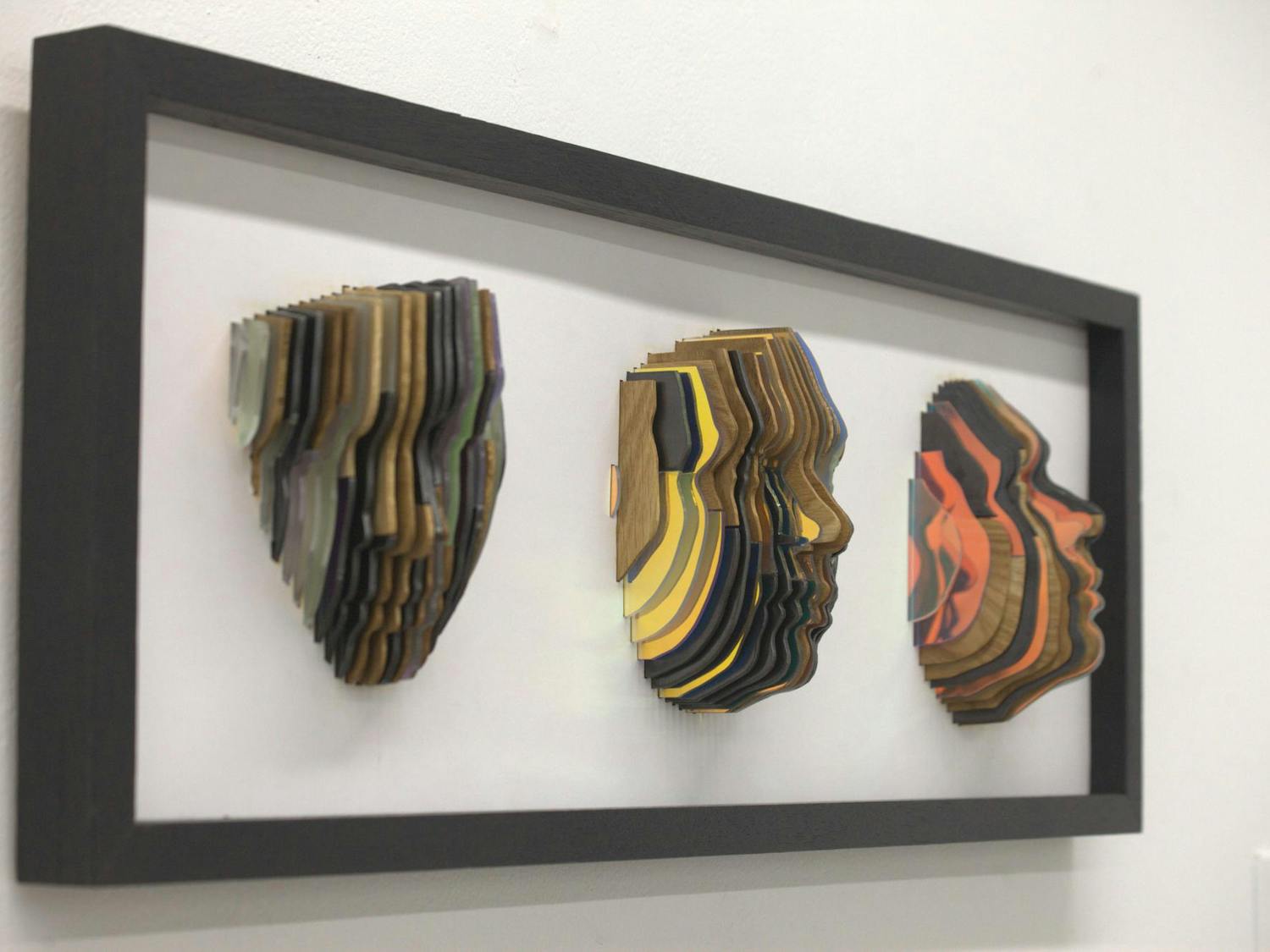 Three faces made of vertical wood, metal, and plastic slices.