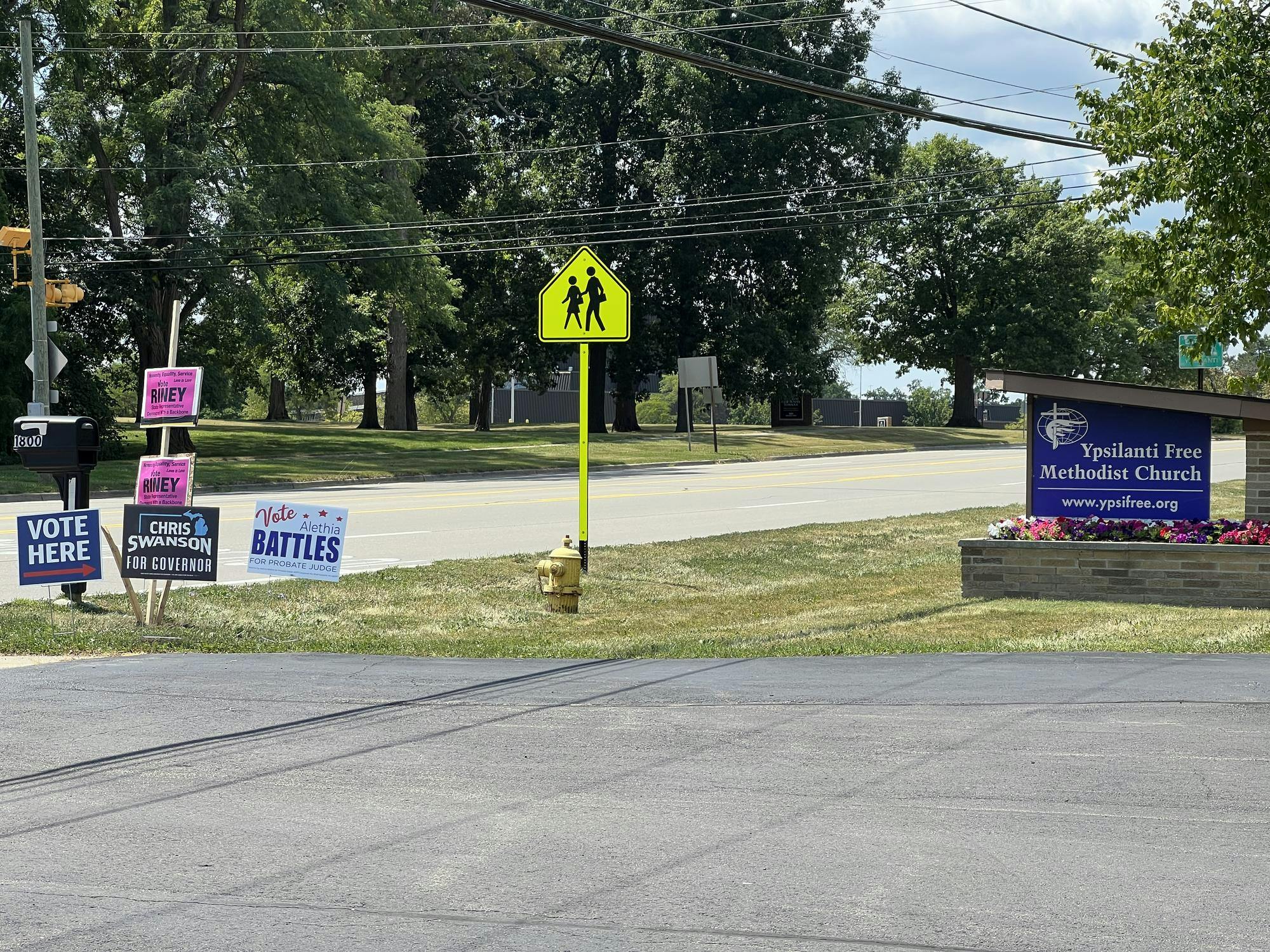 A "vote here" sign sits next to campaign signs for Chris Swanson, Alethia Battles and William Riney near the Ypsilanti Free Methodist Church