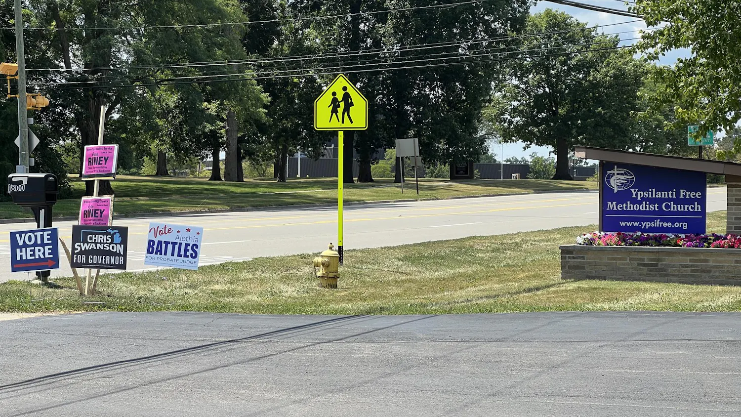 A "vote here" sign sits next to campaign signs for Chris Swanson, Alethia Battles and William Riney near the Ypsilanti Free Methodist Church