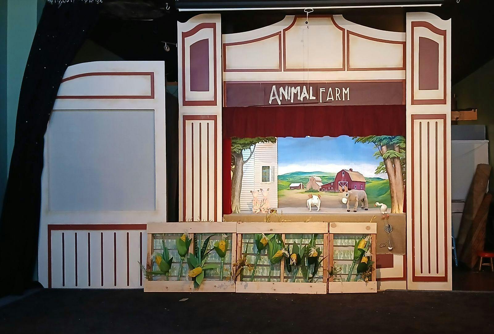 Puppet stage with a farm background and cornfields with three puppets of pigs and one of a horse.