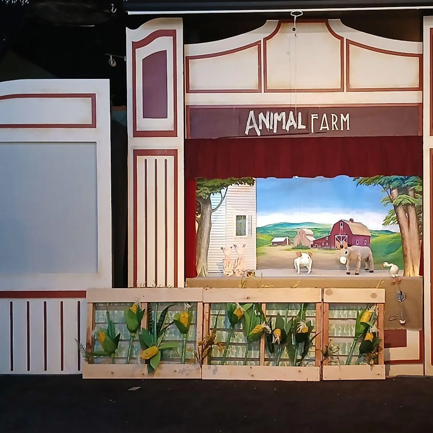Puppet stage with a farm background and cornfields with three puppets of pigs and one of a horse.