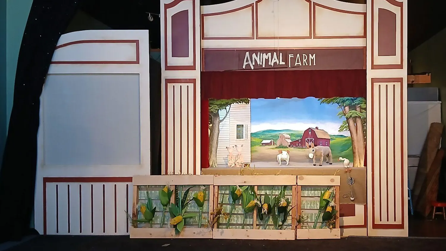 Puppet stage with a farm background and cornfields with three puppets of pigs and one of a horse.