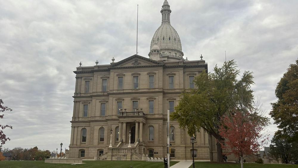 The State Capitol building sits on a grassy lawn next to trees.