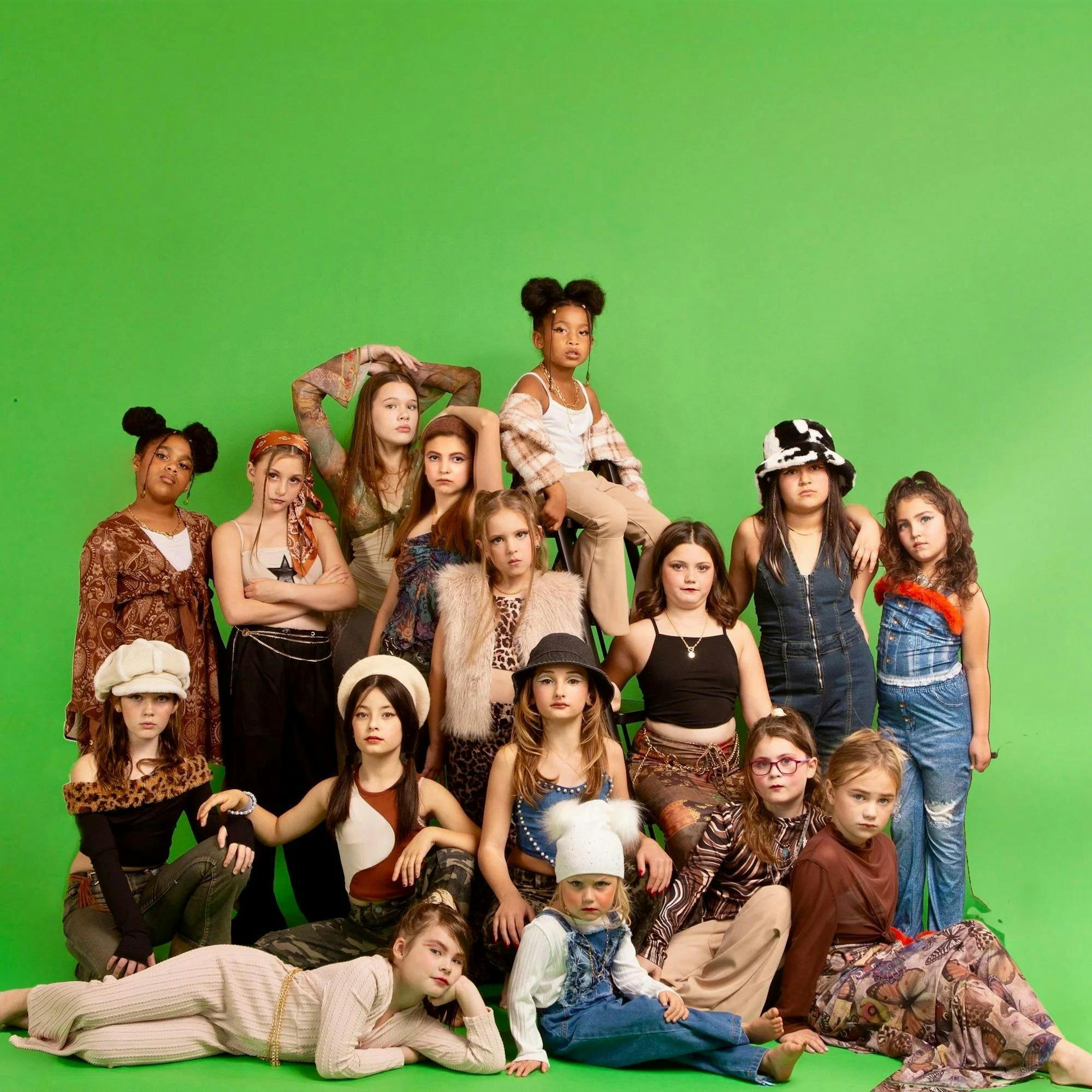 A large group of young girls poses for the photoshoot wearing elaborate outfits with mixed patterns.