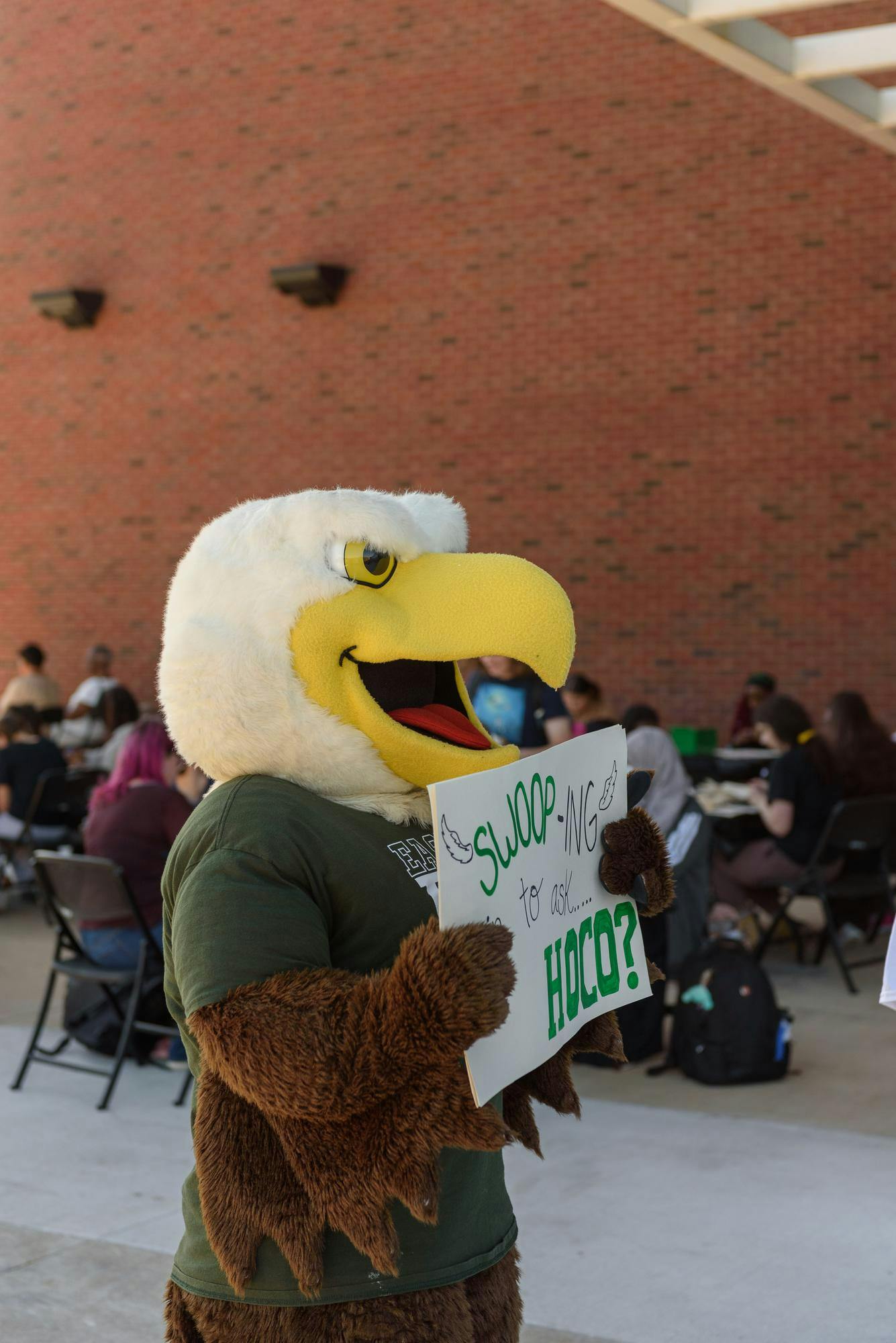 A university mascot holds up a sign to someone.